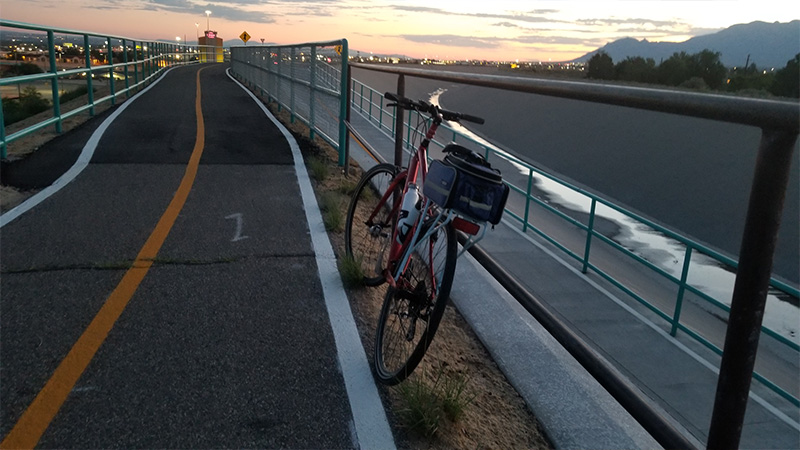 A bike leans up against the railing that separates an arroyo with a paved bike path.