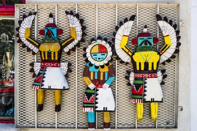 Native American Artwork Three brightly colored Native American wood carvings of people dressed in traditional Native American clothing and feathers, 2 with bird heads and 1 with a round head surrounded by feathers.